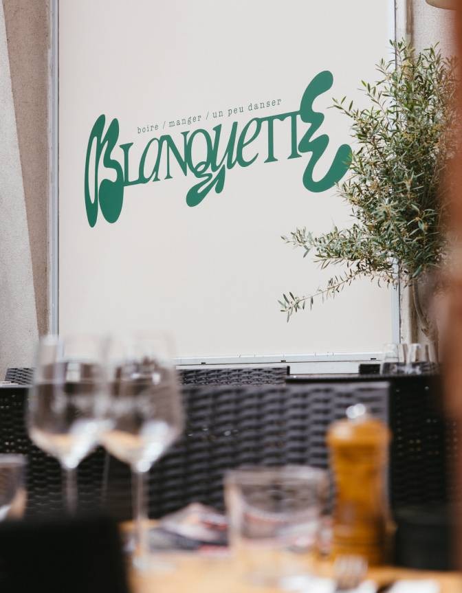 Logo cursif Blanquette en vert sage peint sur le mur intérieur du restaurant, branche d'olivier en avant-plan