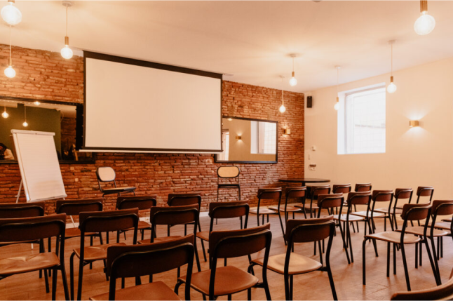 Salle de séminaire au Blanquette : grande table en bois, chaises tapissées, vidéoprojecteur, mur de briques